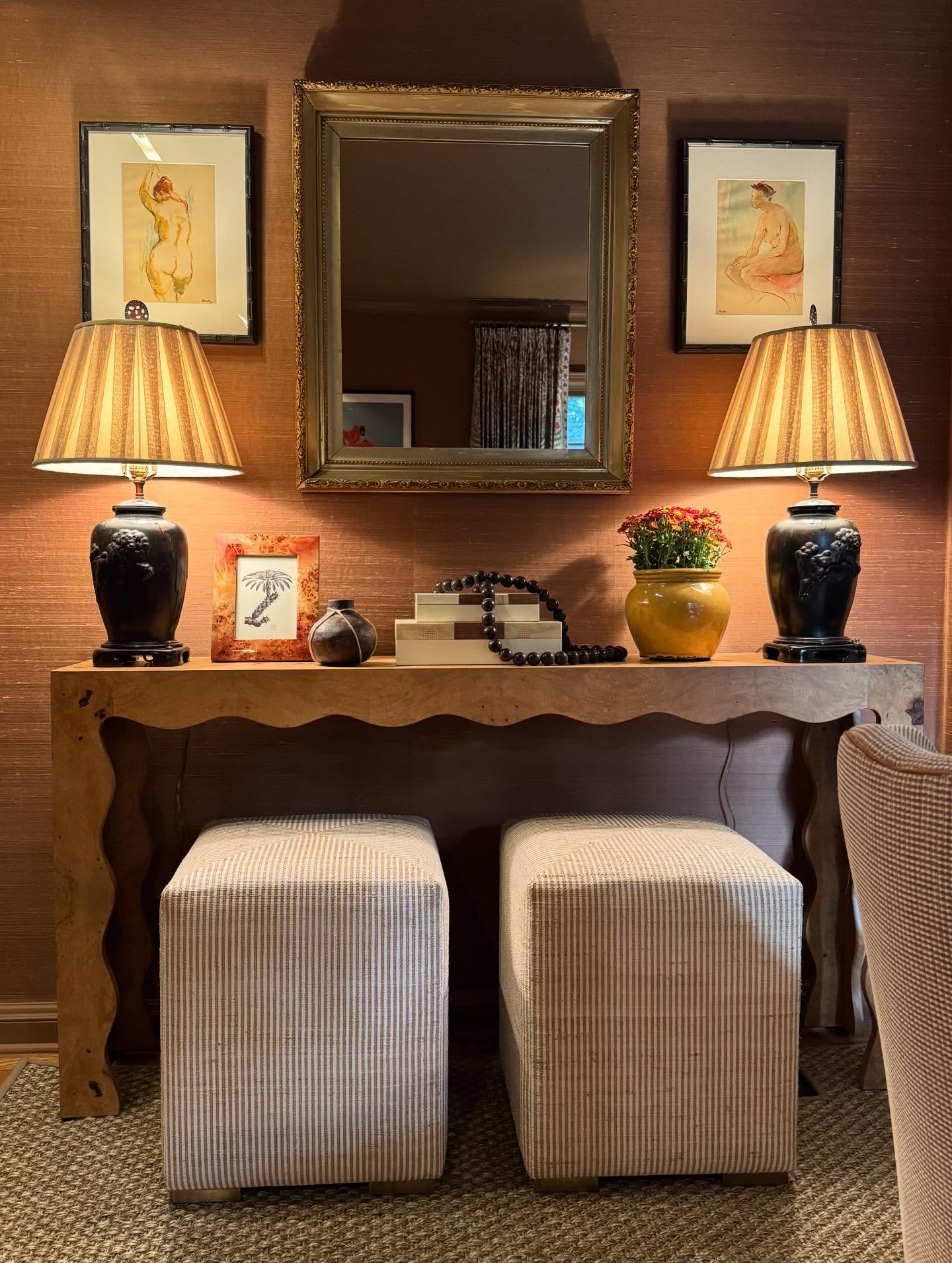 Decorative console table with lamps, mirror, and framed pictures in a room.