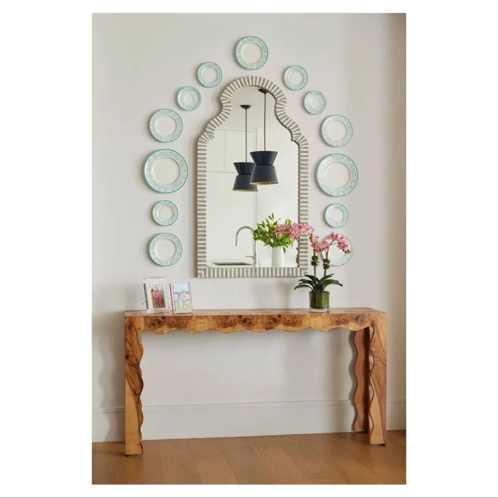 Decorative wall mirror with circular plates and a wooden console table with flowers.