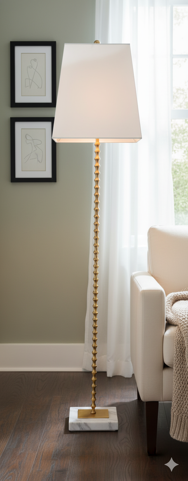 Floor lamp with a white shade in a room with a couch and framed pictures on the wall.